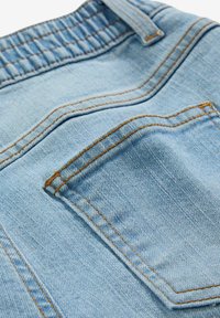Tessuto denim azzurro chiaro con tasca posteriore visibile e cuciture arancioni, che mostrano texture e dettagli in materiale chambray.