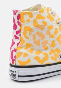 Wysokie trampki z płótna z białą podstawą i żółtymi oraz różowymi plamkami w cętki, czarną gumową podeszwą i okrągłą łatą z logo.