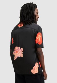 Kortermet svart skjorte med levende blomstertrykk i rødt og rosa, laget av glatt stoff med en avslappet passform og rett kant.