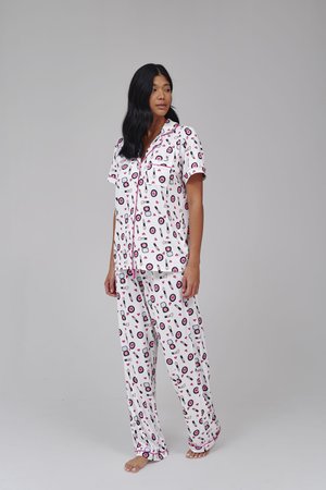 Vrouw staat blootsvoets en draagt een wit pyjamaset met roze en zwarte make-up print op een effen lichtgrijze achtergrond.