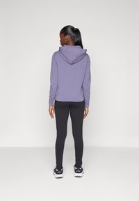 Ljubičasta hoodie s velikom kapuljačom, uparen s crnim tajicama i atletskim cipelama; glatka tekstura, prilagođen dizajn i istaknuti detalji šivanja.