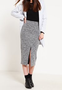 Grå stickad pennkjol med en framslits, ihopkopplad med en svart topp och en lång vit blazer. Svarta ankelskor fulländar looken.