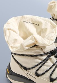 Lekkie buty z kremową termoizolacyjną podszewką, czarnymi akcentami, teksturowanym materiałem oraz elastycznymi sznurowadłami zapewniającymi pewne dopasowanie.