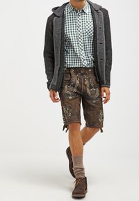 Donkergrijze trui met een capuchon, groen en witte geruite shirt, en bruine lederhosen met bloemmotieven. Bruine enkellaarsjes en grijze sokken.