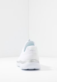 Scarpa da ginnastica bianca con tomaia in rete testurizzata, una decorazione argentata sul tallone e una suola liscia e ammortizzata. La vista posteriore mette in evidenza il design.
