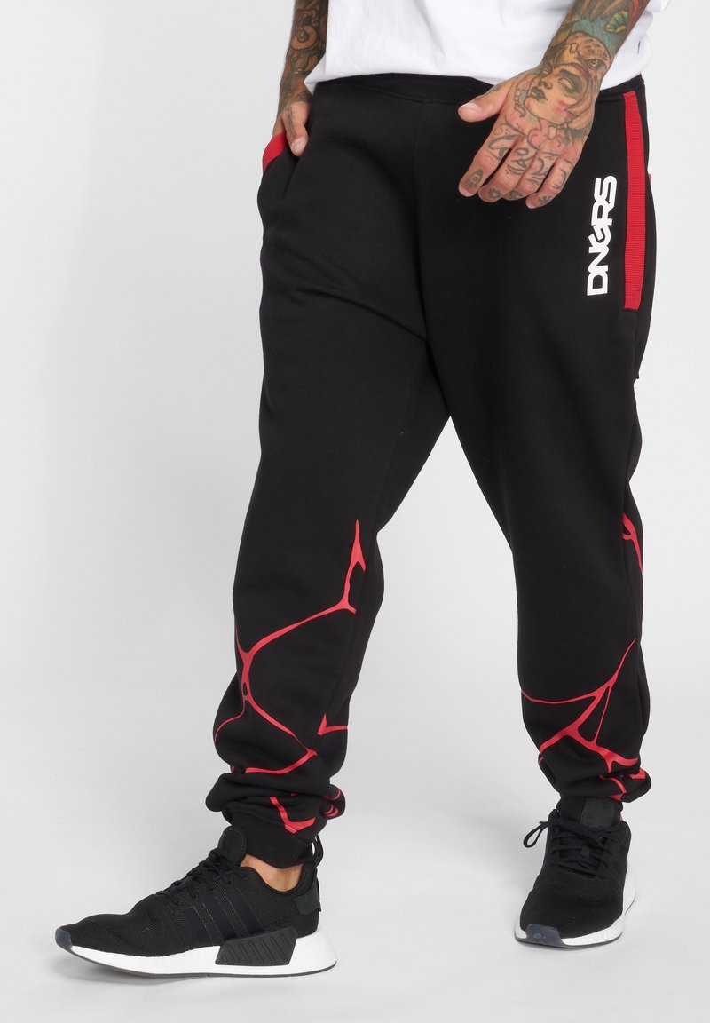 Black sweatpants with red accents, elastic waistband, and abstract red pattern. Paired with black athletic shoes featuring white soles.