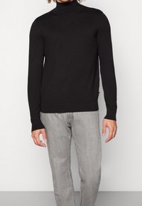 Musta poolhigh-neule sopusuhtaisessa designissa, valmistettu sileästä kankaasta, pitkät hihat ja ribbaus helmassa. Yhdistetty harmaisiin farkkuihin.