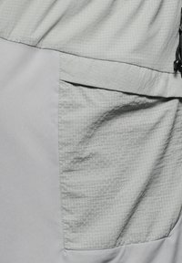 Ljust grå plagg med en texturerad tyg med rutförmning. Inkluderar en stor sidoficka och en rynkad midja med dragsko.