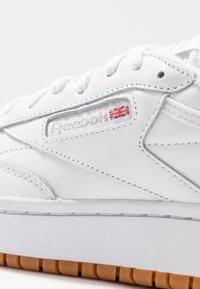 Vita lädersneaker med texturerad yta, Reebok-logga och Union Jack-detalj på sidan, samt en gummisula.