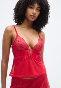 Camisole en satin rouge et dentelle avec un profond col en V, fines bretelles et détails en dentelle ornée ; silhouette fluide avec des détails de design superposés.