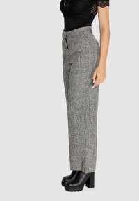 Pantaloni grigio testurizzati con una vestibilità su misura, vita alta e una finitura liscia. Indossati con stivaletti neri con tacco a piattaforma.