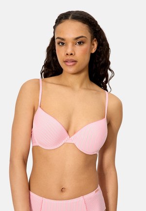 Mujer con cabello rizado que lleva un sujetador a rayas rosas y blancas y braguitas de cintura alta a juego, mirando hacia adelante contra un fondo liso.