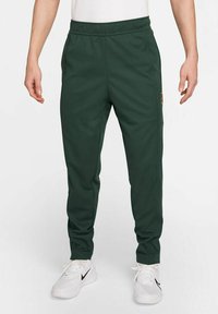 Pantalones deportivos de color verde oscuro, fabricados con un tejido suave, que cuentan con una cintura elástica, bolsillos laterales y un parche de logo en el muslo.