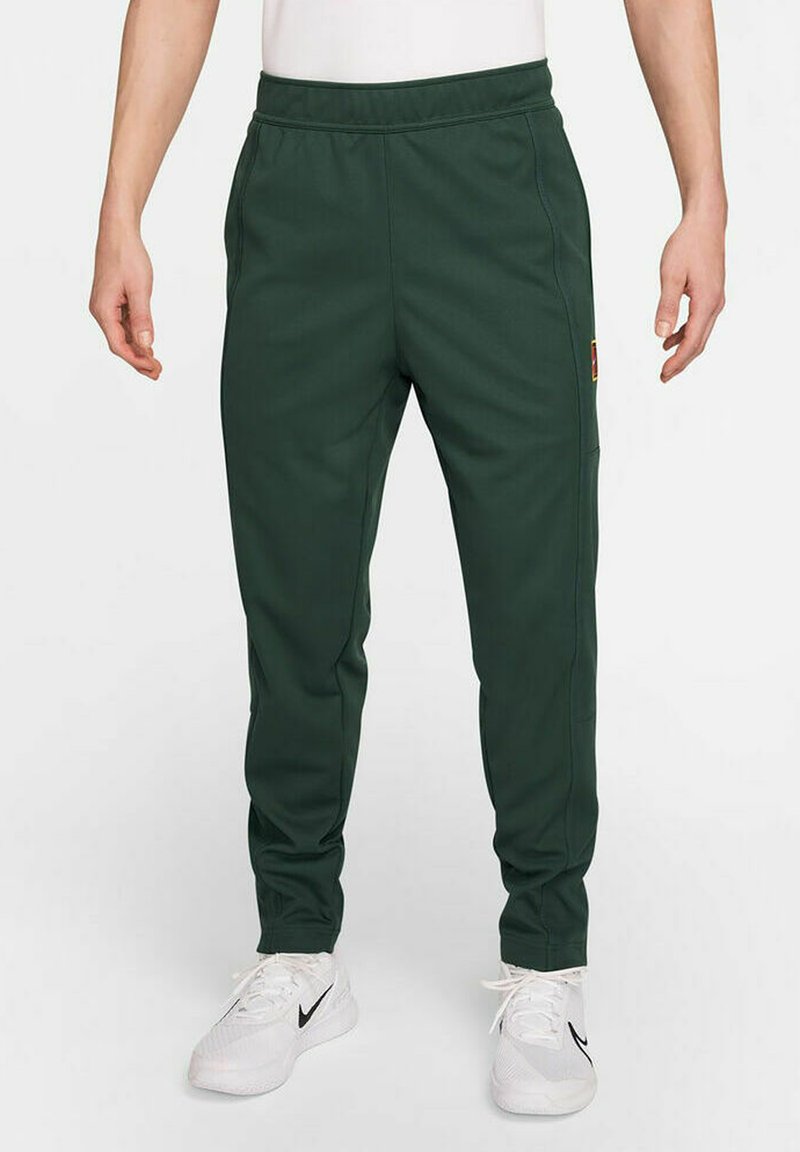 Pantalones deportivos de color verde oscuro, fabricados con un tejido suave, que cuentan con una cintura elástica, bolsillos laterales y un parche de logo en el muslo.