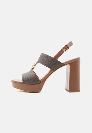 Brown platform sandal with thick block heel, adjustable ankle strap, wide textured front straps, and gold decorative emblem on side.