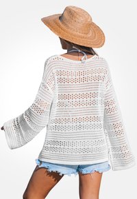 Pull en tricot blanc avec de grands mailles ouvertes et un design ample et fluide. Il possède des manches longues et une coupe décontractée, associé à un short en denim.