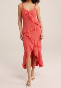 Coral dress with ruffled detailing, thin straps, and a knee-high slit. Made from lightweight fabric with a flowing silhouette.