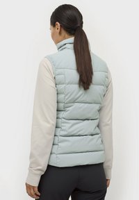 Lichtblauwe puffervest met een hoge kraag, voorzien van horizontale gestikte secties en een soepele textuur, gedragen over een lichtgekleurde langetermijn-shirt.
