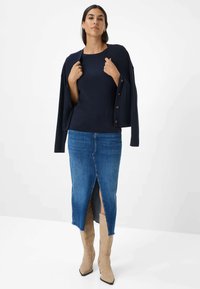 Maglione a coste blu navy indossato sotto un cardigan coordinato, abbinato a una gonna di jeans di lunghezza media con uno spacco frontale e stivali beige a punta.