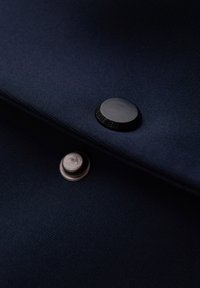 Tissu bleu foncé avec un bouton-pression métallique partiellement fermé, montrant les parties mâle et femelle du bouton.