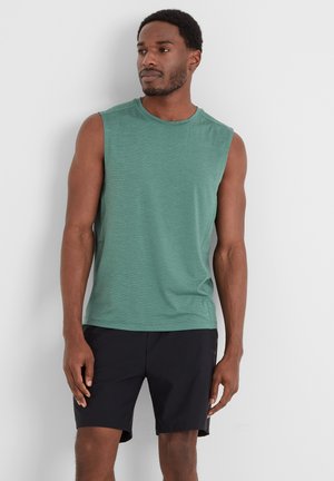 Sleeveless green shirt made of lightweight fabric, featuring a round neckline. Worn with black shorts, showing smooth texture and simple design.