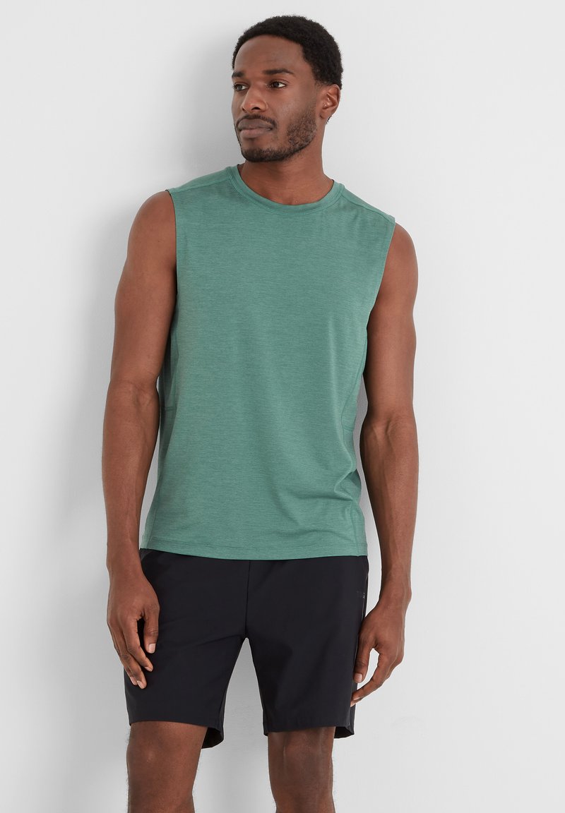 Sleeveless green shirt made of lightweight fabric, featuring a round neckline. Worn with black shorts, showing smooth texture and simple design.