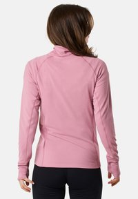 Haut à manches longues rose clair avec col montant, en tissu texturé, et avec des orifices pour les pouces, comportant des coutures plates et une silhouette ajustée.