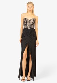Zwarte strapless jurk met kant bodice, getailleerd ontwerp en vloeiende rok met een hoge split en textuurstof. Minimalistische sandaaltjes met bandjes.