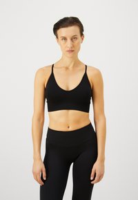Sostén deportivo negro con tirantes finos y un profundo diseño de escote en V, combinado con leggings negros de cintura alta, ambos con una textura suave.
