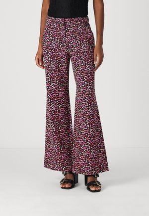 Vrouw draagt zwarte broek met wijde pijpen en roze, witte en bruine bloemenprint, gecombineerd met zwarte sandalen met open teen en hak.