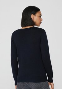 Granatowy sweter z dzianiny z prążkowanym dołem i mankietami, z okrągłym dekoltem i długimi rękawami, przedstawiony z tyłu.