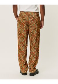 Kordfløyelsbukser med et flerfarget blomsterdesign i rødt, grønt og beige. Rett ben-design med to baklommer.