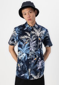 Chemise à manches courtes bleu marine avec un imprimé de palmier tropical et d'oiseaux. Fabriquée en tissu léger, elle dispose d'une patte de boutonnage à l'avant et d'un col.