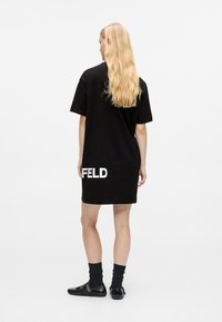 Crna pamučna haljina majica s kratkim rukavima, s bijelim otiskom "FELD" blizu rubova. Glatka tekstura i opušteni kroj.