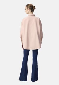 Långärmad, ljusrosa skjorta med krage, tillsammans med mörkblå utsvängda jeans; slät textur och avslappnad passform.