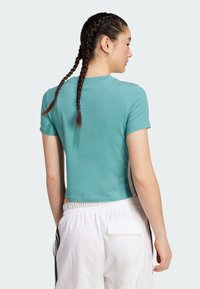 Turkos kortärmad t-shirt med rund halsringning och korta ärmar, tillverkad av ett mjukt tyg. Bärs tillsammans med vita byxor med elastisk midja och sidostripes.