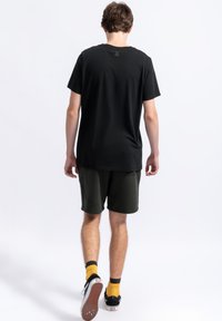 Zwart katoenen T-shirt met een ronde hals, gecombineerd met olijfgroene shorts, gele en zwarte sokken, en zwarte sneakers met een witte zool.