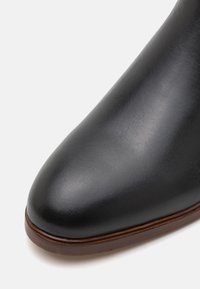 Černá kožená bota s hladkým, polos lesklým povrchem. Kulatý špička a hnědý kožený akcent na podrážce. Minimalistický design.