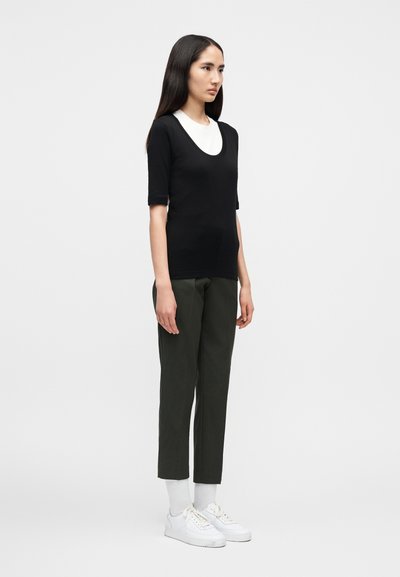 Μαύρο κοντομάνικο τοπ με λευκή λαιμόκοψη σε σχήμα scoop, συνδυασμένο με σκούρο πράσινο παντελόνι με στενή γραμμή και λευκά αθλητικά παπούτσια με παχιά σόλα.