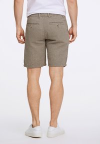 Pantalones cortos de espiga marrón con un corte recto, dos bolsillos traseros y dobladillo vuelto, combinados con zapatillas blancas. La textura de la tela es suave.