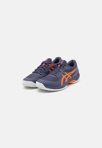 Baskets de sport violettes avec des accents orange, tige en mesh, semelle rembourrée et semelle extérieure en caoutchouc texturé. Comprend des lacets et des détails de marque.