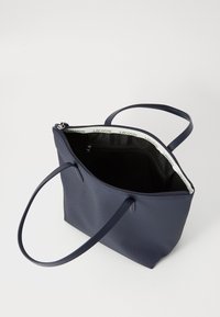 Navy blue tote bag made of textured material, featuring a zip closure, two handles, and a black interior with a logo-printed trim.