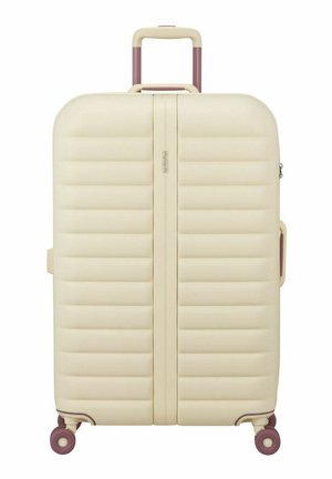 Valise rigide couleur crème avec des rainures horizontales, poignée rétractable, poignée latérale et quatre roues pivotantes violettes.