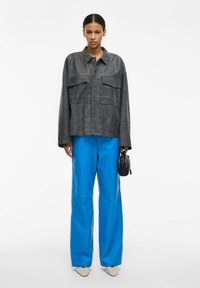 Üle suurusega hall anteülikond kahe rinnataskuga, kombineeritud erk siniste laiade nahapükstega. Modell hoiab väikest musta käekotti.