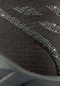 Schwarzer Sportschuh mit einem strukturierten Mesh-Obermaterial und einem eleganten Design. Verfügt über eine Gummisohle mit geriffelten Akzenten für besseren Halt.