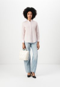 Una camicia a maniche lunghe di un leggero rosa con colletto abbottonato, abbinata a jeans blu larghi e una piccola borsa a tracolla bianca e testurizzata. Tacchi neri completano l'outfit.