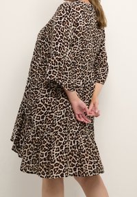 Vestido de estampado de leopardo con dobladillo en capas, mangas largas y un corte holgado. Fabricado con un tejido suave que presenta manchas marrones, negras y rojas.