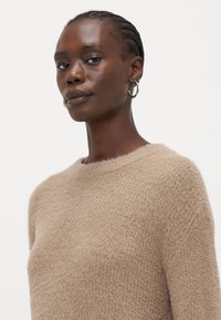 Maglione beige chiaro realizzato in materiale morbido e peloso, con collo tondo e vestibilità comoda. Caratterizzato da cuciture minime e una finitura testurizzata.
