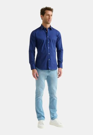 Maglietta a maniche lunghe blu navy con colletto button-down, abbinata a jeans azzurri e sneakers bianche. Tessuto morbido, design aderente.