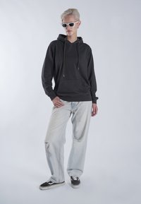 Fekete pamut kapucnis pulóver zsinórral, elülső zsebbel. Világoskék, kopott hatású farmernadrág lyukakkal. Fekete tornacipő fehér talppal.